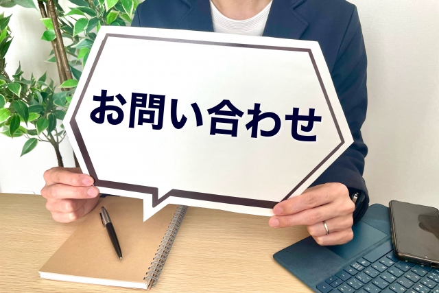 「お問い合わせ」と書かれたボードを手に持つスタッフのイメージ